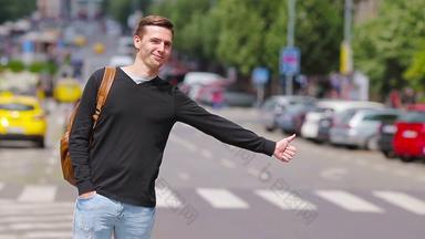 年轻的快乐男人。抓出租车欧洲街道肖像高加索人旅游背包微笑捕捉出租车